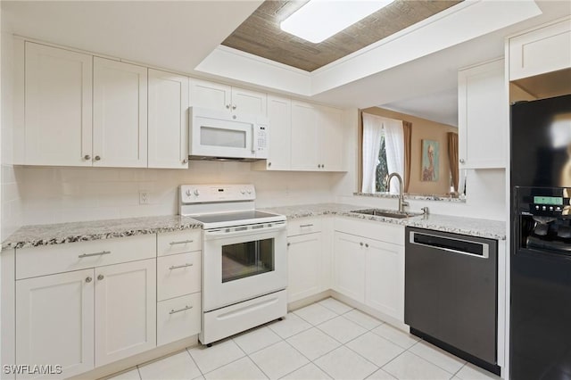 kitchen with white appliances, sink, a tray ceiling, light tile patterned flooring, and white cabinetry