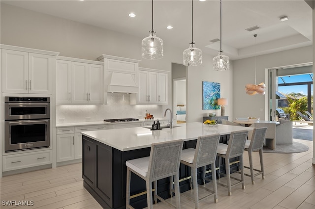 kitchen featuring white cabinetry, sink, stainless steel double oven, a large island with sink, and decorative light fixtures