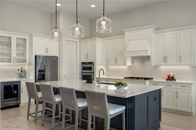 kitchen with a high ceiling, sink, an island with sink, white cabinetry, and beverage cooler