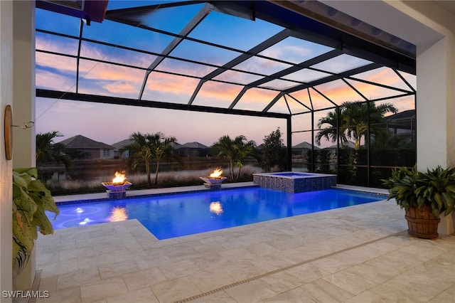 pool at dusk with an in ground hot tub, pool water feature, glass enclosure, an outdoor fire pit, and a patio