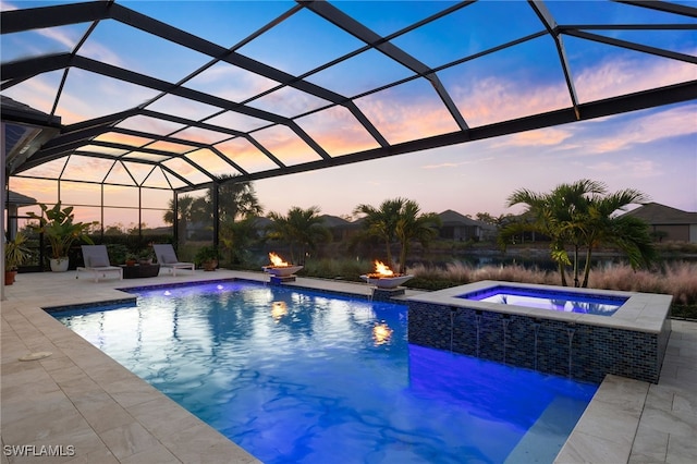 pool at dusk with glass enclosure, pool water feature, an in ground hot tub, a patio area, and an outdoor fire pit