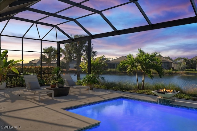 pool at dusk featuring a lanai, pool water feature, a water view, a fire pit, and a patio