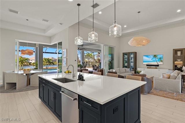 kitchen with a tray ceiling, stainless steel dishwasher, hanging light fixtures, and sink