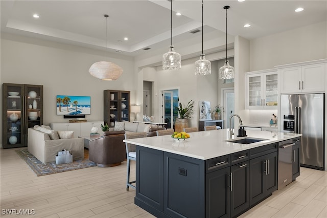 kitchen featuring stainless steel appliances, a tray ceiling, sink, pendant lighting, and white cabinetry