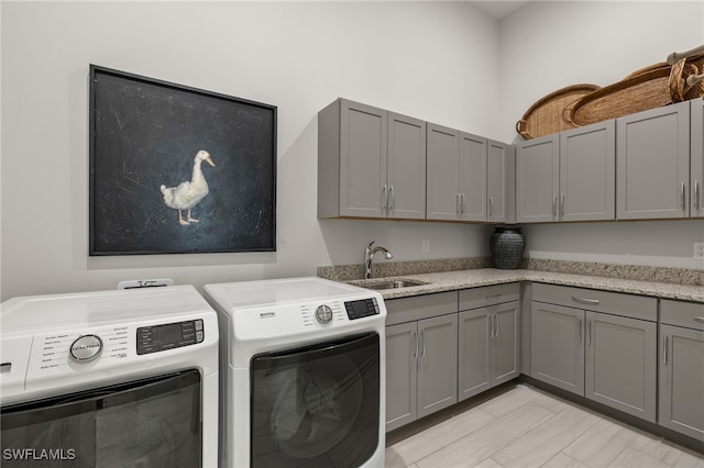 clothes washing area with separate washer and dryer, sink, and cabinets