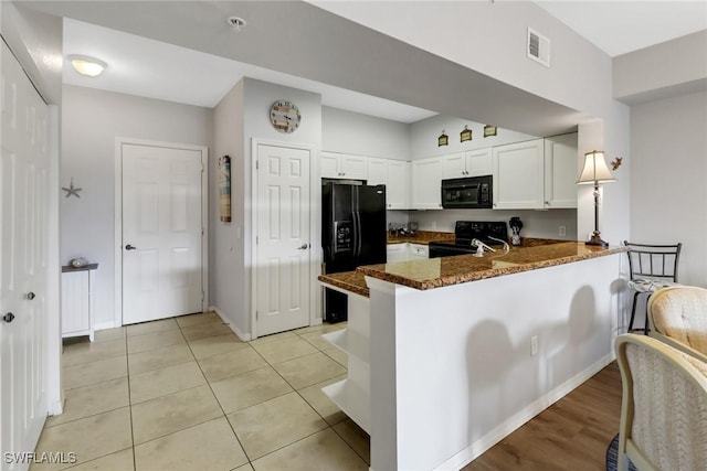 kitchen with black appliances, kitchen peninsula, dark stone countertops, light tile patterned flooring, and white cabinetry