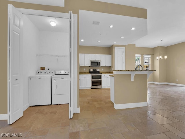 kitchen with washer and clothes dryer, a breakfast bar, hanging light fixtures, appliances with stainless steel finishes, and white cabinetry