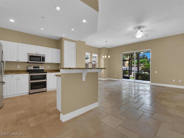 kitchen featuring pendant lighting, white cabinets, a center island with sink, appliances with stainless steel finishes, and a kitchen bar