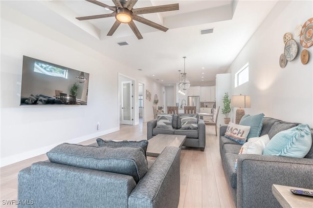 living room with ceiling fan, a tray ceiling, and light hardwood / wood-style flooring