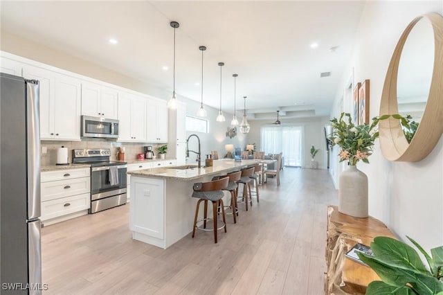 kitchen featuring light stone countertops, stainless steel appliances, pendant lighting, white cabinetry, and an island with sink