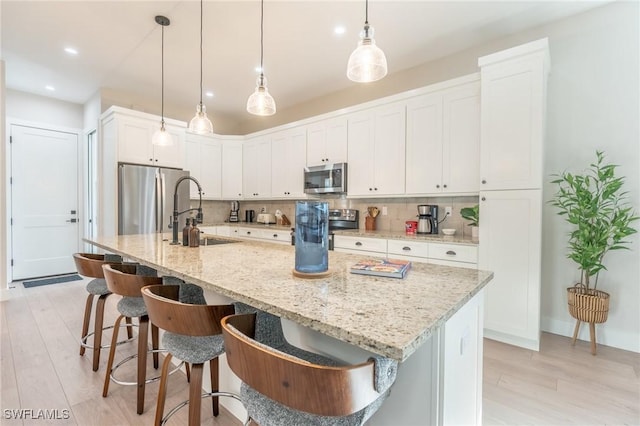 kitchen featuring tasteful backsplash, white cabinets, an island with sink, and appliances with stainless steel finishes