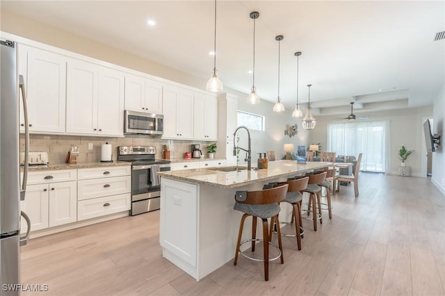 kitchen featuring pendant lighting, a center island with sink, ceiling fan, appliances with stainless steel finishes, and white cabinetry