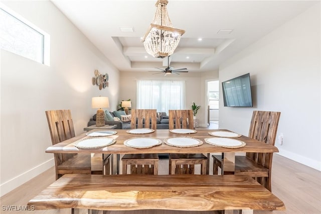 dining area with ceiling fan with notable chandelier, a raised ceiling, and light hardwood / wood-style flooring