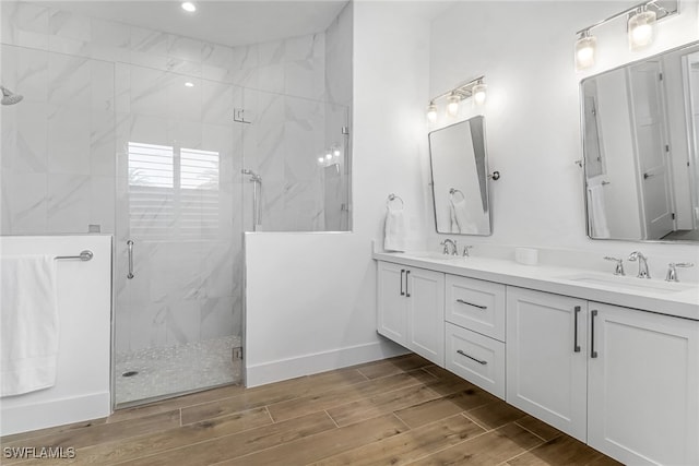 bathroom featuring a sink, double vanity, wood finish floors, and a marble finish shower