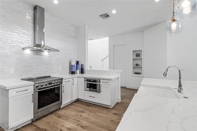 kitchen with stainless steel appliances, a sink, visible vents, wall chimney range hood, and light wood finished floors