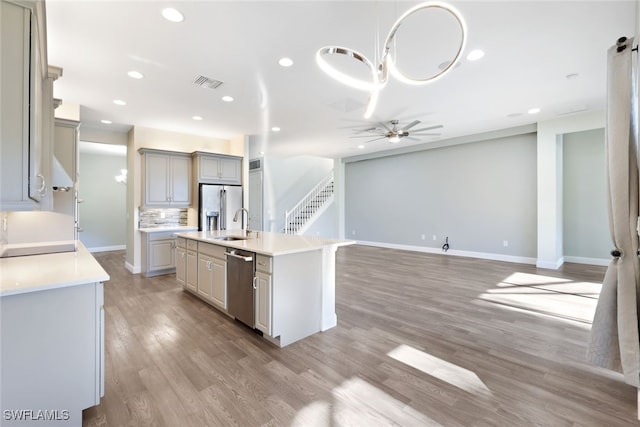 kitchen with gray cabinetry, a kitchen island with sink, light wood-type flooring, appliances with stainless steel finishes, and tasteful backsplash