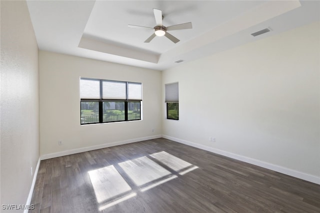 unfurnished room featuring ceiling fan, dark wood-type flooring, and a tray ceiling