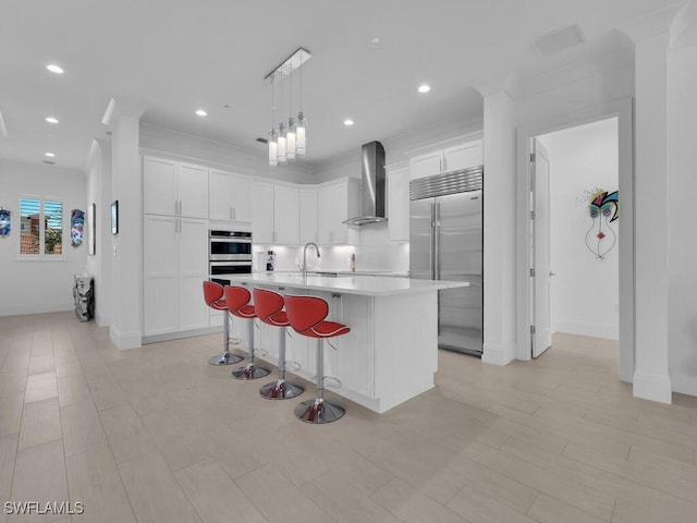 kitchen with appliances with stainless steel finishes, a center island with sink, white cabinetry, and wall chimney exhaust hood