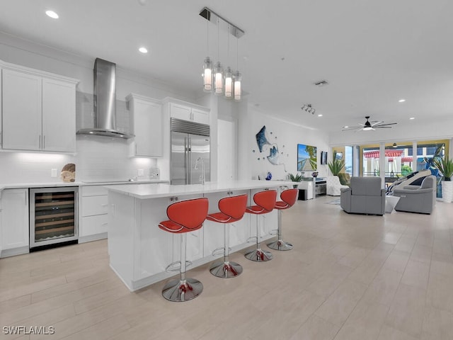 kitchen with built in fridge, white cabinets, wall chimney range hood, and wine cooler