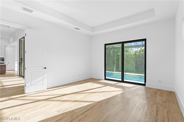 unfurnished room with light wood-type flooring and a tray ceiling