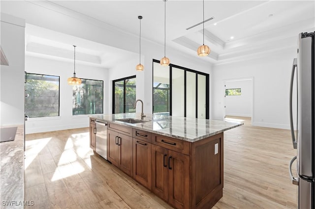 kitchen featuring a tray ceiling, a kitchen island with sink, hanging light fixtures, and stainless steel appliances