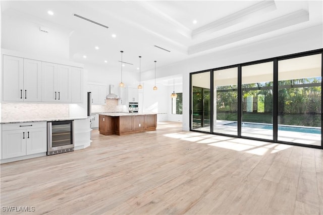 kitchen featuring decorative backsplash, beverage cooler, a spacious island, pendant lighting, and white cabinets