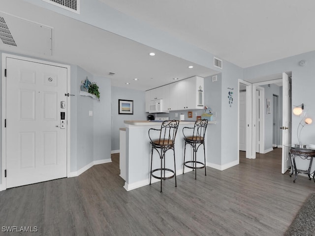 kitchen featuring kitchen peninsula, white cabinetry, a breakfast bar, and dark hardwood / wood-style floors