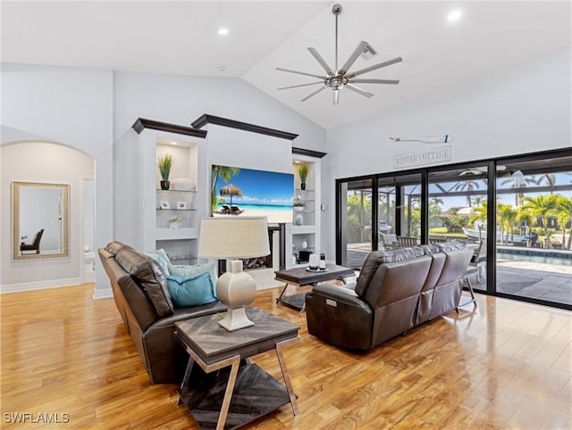 living room with ceiling fan, built in features, a towering ceiling, and light hardwood / wood-style flooring