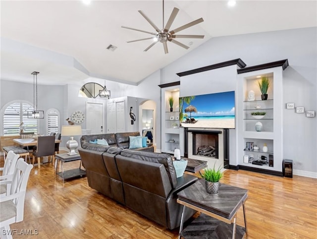 living room with ceiling fan with notable chandelier, light hardwood / wood-style floors, built in features, and vaulted ceiling