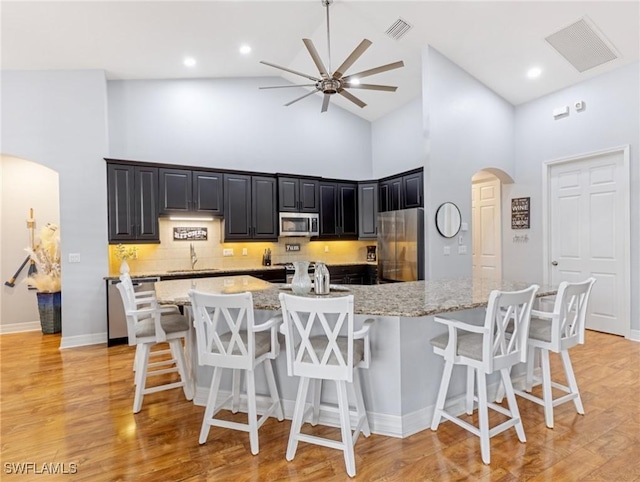 kitchen featuring high vaulted ceiling, a kitchen bar, sink, and appliances with stainless steel finishes