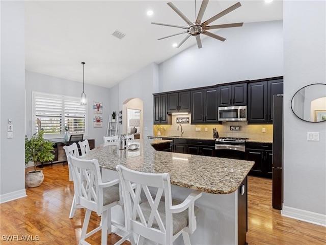 kitchen with appliances with stainless steel finishes, tasteful backsplash, light stone counters, a breakfast bar, and decorative light fixtures