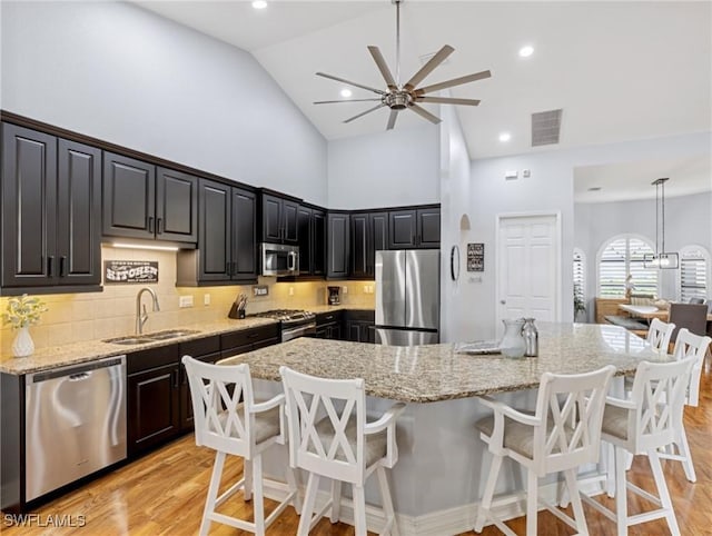 kitchen with high vaulted ceiling, sink, ceiling fan, appliances with stainless steel finishes, and a kitchen bar