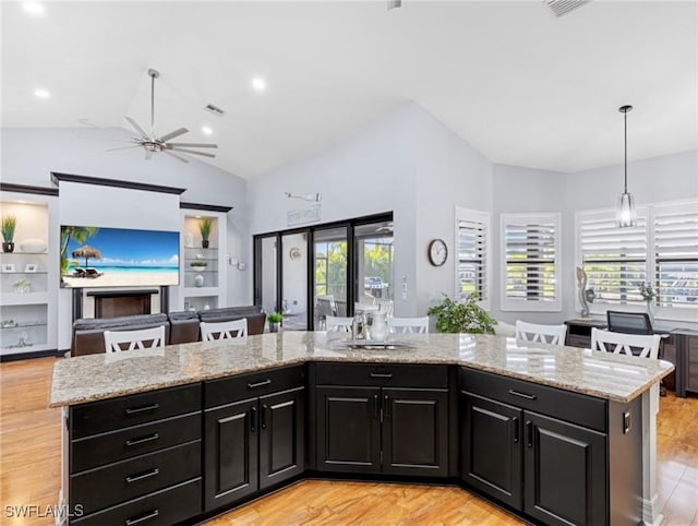 kitchen featuring vaulted ceiling, ceiling fan, decorative light fixtures, a kitchen island, and light stone counters