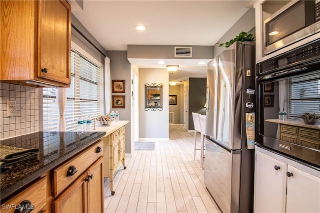 kitchen with dark stone countertops, decorative backsplash, light hardwood / wood-style floors, and appliances with stainless steel finishes