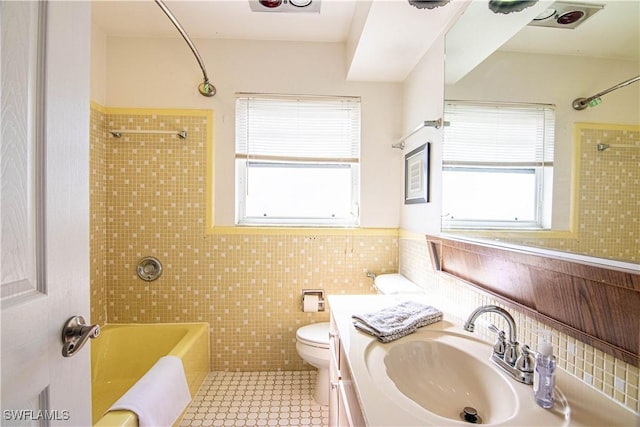 full bathroom with vanity, tile patterned floors, tiled shower / bath combo, toilet, and tile walls