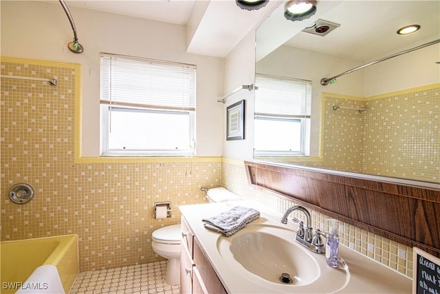 full bathroom with tile patterned floors, vanity, tiled shower / bath combo, tile walls, and toilet