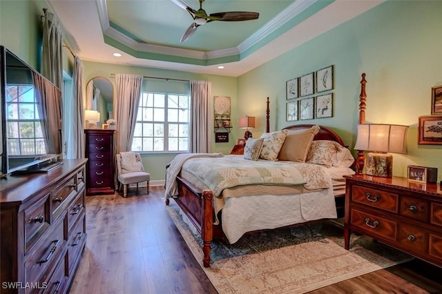 bedroom featuring ceiling fan, a raised ceiling, ornamental molding, and wood-type flooring