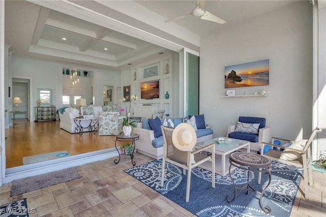 living room featuring a fireplace, coffered ceiling, ceiling fan with notable chandelier, beamed ceiling, and a high ceiling