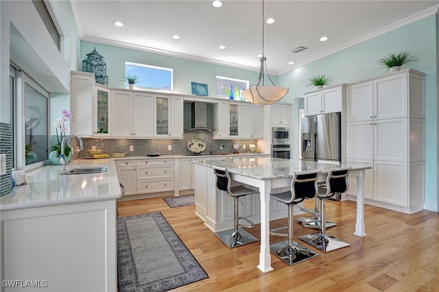 kitchen featuring appliances with stainless steel finishes, sink, wall chimney range hood, decorative light fixtures, and white cabinetry