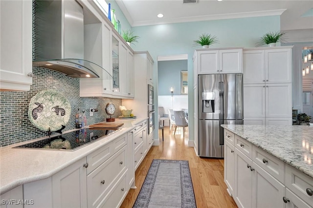 kitchen with white cabinets, wall chimney range hood, ornamental molding, and appliances with stainless steel finishes