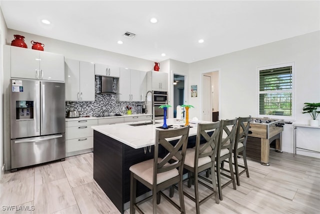 kitchen featuring white cabinetry, stainless steel appliances, tasteful backsplash, a breakfast bar, and a center island with sink