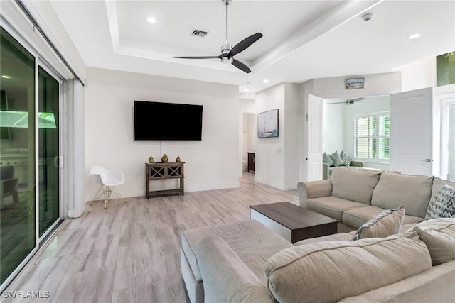 living room with ceiling fan, light wood-type flooring, and a tray ceiling