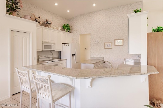 kitchen featuring kitchen peninsula, a kitchen breakfast bar, white appliances, light tile patterned floors, and white cabinets