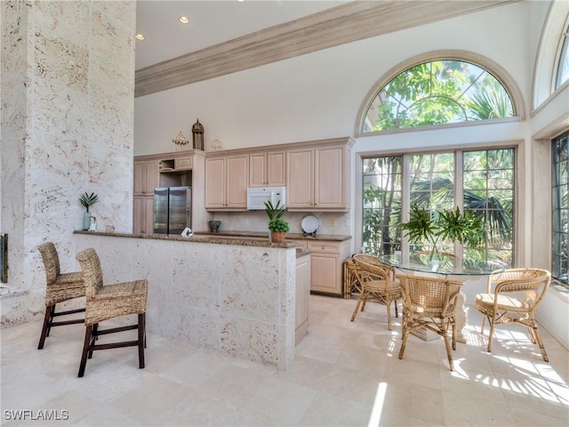 kitchen with light brown cabinetry, crown molding, stainless steel refrigerator, a high ceiling, and kitchen peninsula