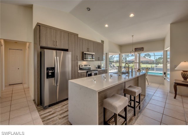 kitchen with a center island with sink, light tile patterned flooring, appliances with stainless steel finishes, and vaulted ceiling