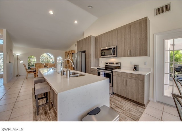 kitchen featuring a healthy amount of sunlight, vaulted ceiling, an island with sink, light tile patterned flooring, and stainless steel appliances