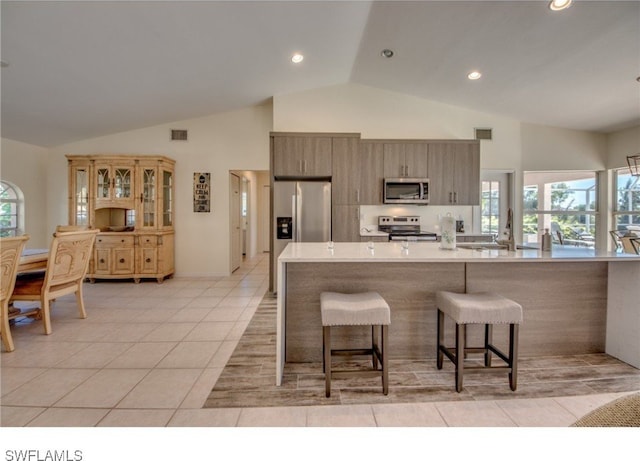 kitchen with a kitchen bar, light tile patterned floors, stainless steel appliances, and high vaulted ceiling