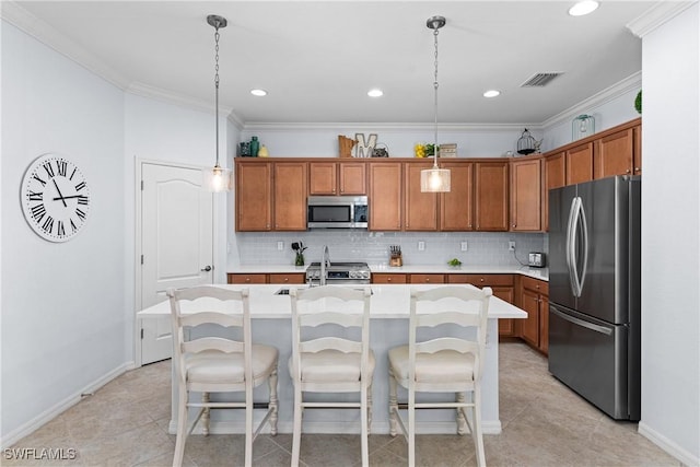 kitchen with pendant lighting, crown molding, appliances with stainless steel finishes, a kitchen island with sink, and a kitchen bar