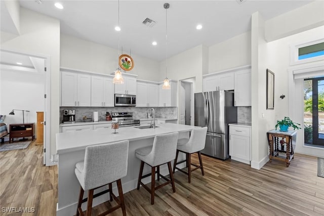 kitchen with a kitchen island with sink, sink, hanging light fixtures, white cabinetry, and stainless steel appliances