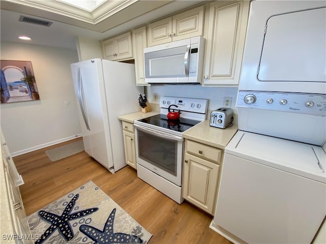 kitchen featuring cream cabinets, white appliances, light hardwood / wood-style floors, and stacked washer / dryer